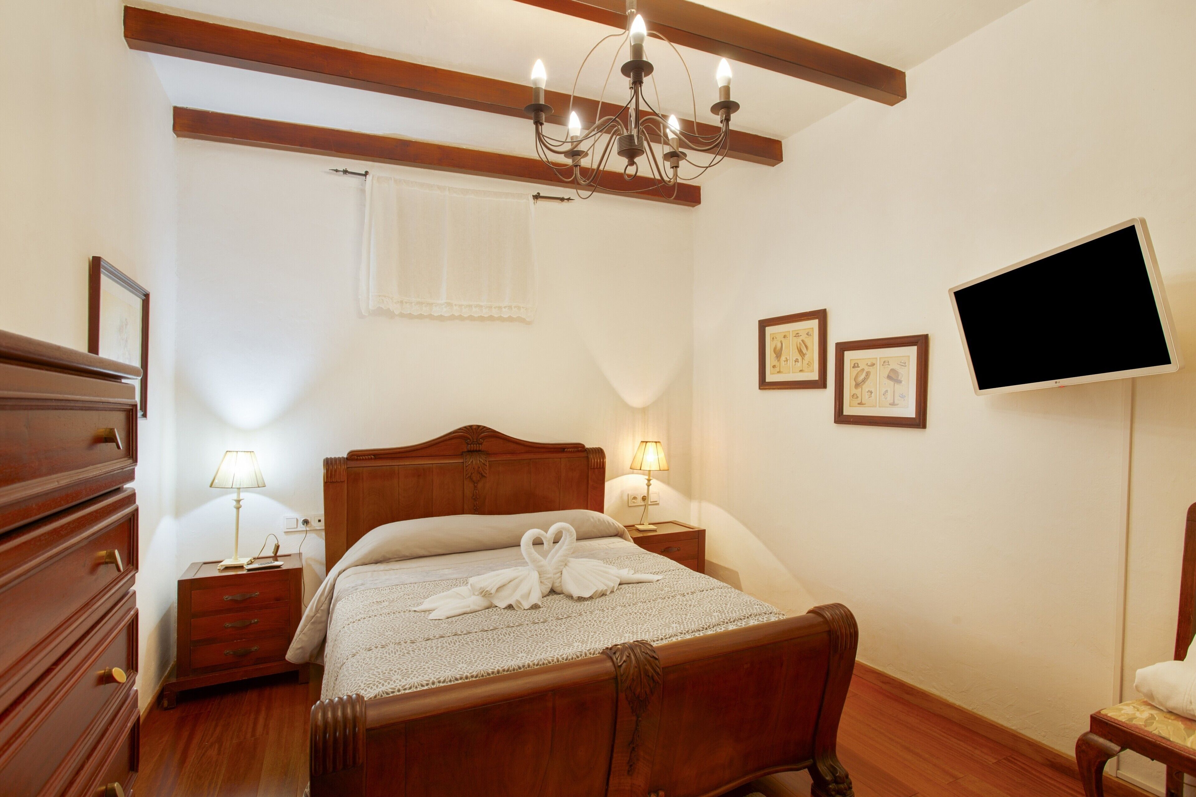 Un dormitorio con una cama de madera, lámparas de noche, un televisor de pantalla plana y una araña.