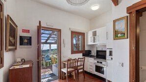 Cocina compacta con armarios de madera, una mesa de comedor con sillas y vistas a un espacio exterior a través de un ventanal abierto.