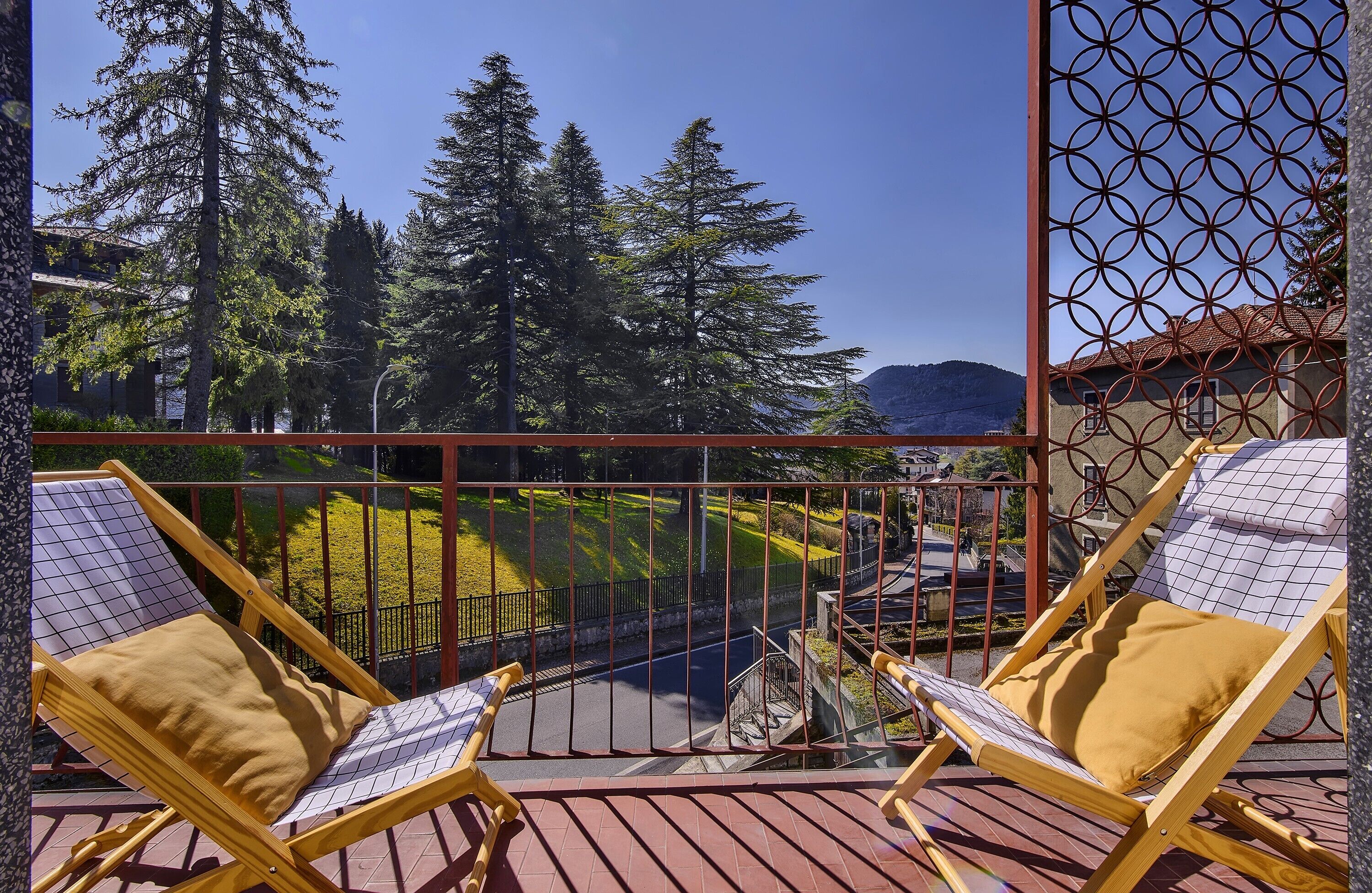 Ein Balkon mit zwei Holzliegen, einem Metallgeländer und Blick auf Bäume und ein Gebäude.