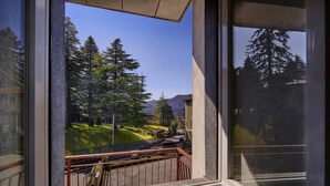 Blick aus einem Fenster mit Balkon, der eine Landschaft mit Bäumen und einem fernen Berg zeigt.