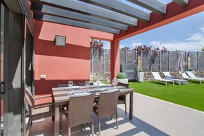 An outdoor patio with a table set for dining, wicker chairs, and a view of a well-maintained lawn and fence. - Holiday Villa 'Alexandria's Retreat' with Sea Views, Wi-Fi and Air Conditioning (San Bartolome de Tirajana)