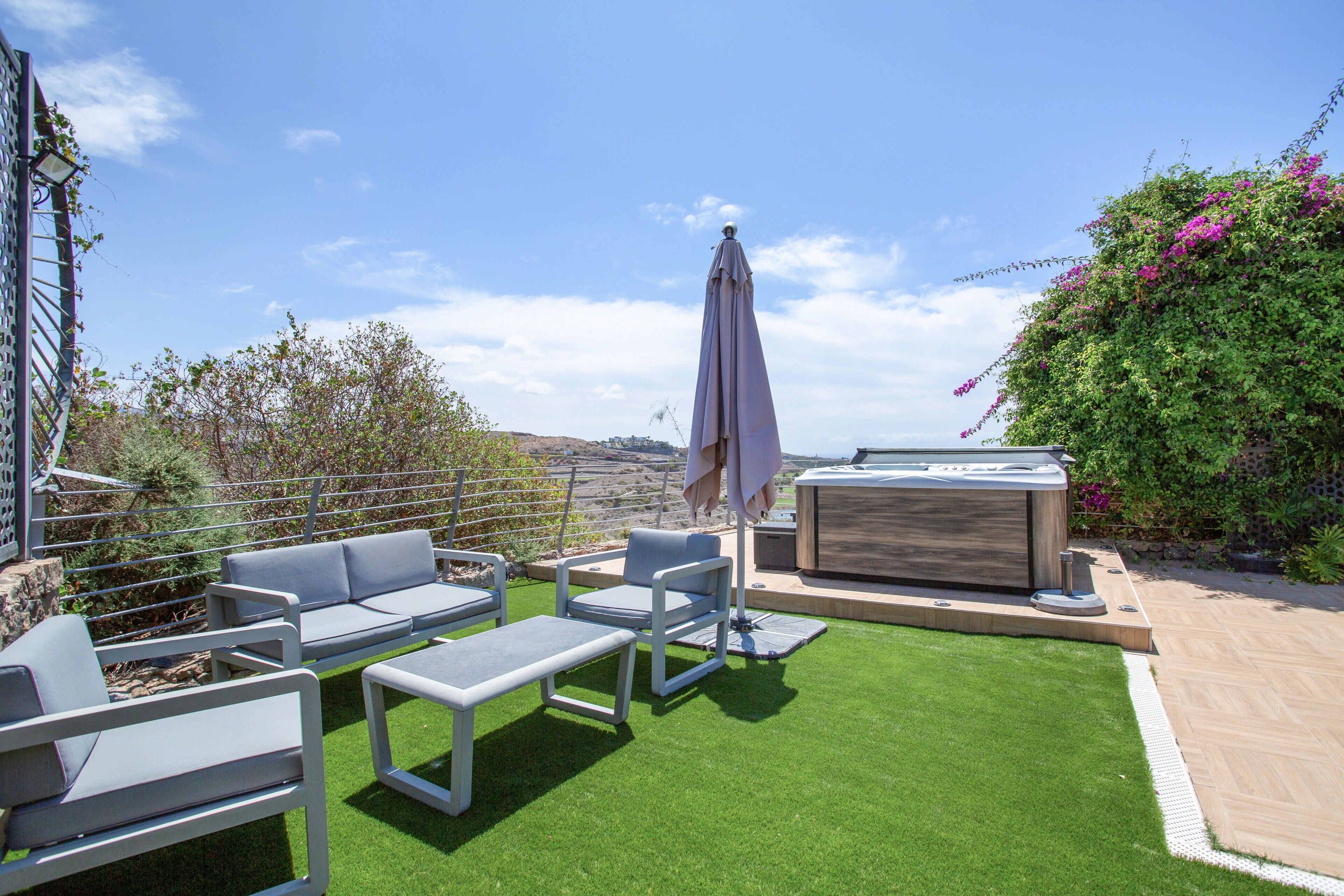 Een terras buiten met een loungeset, een tafel en een parasol.