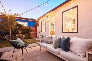 Eine moderne Außenpatio mit einem weißen Sofa, einem Korbstuhl und Lichterketten.