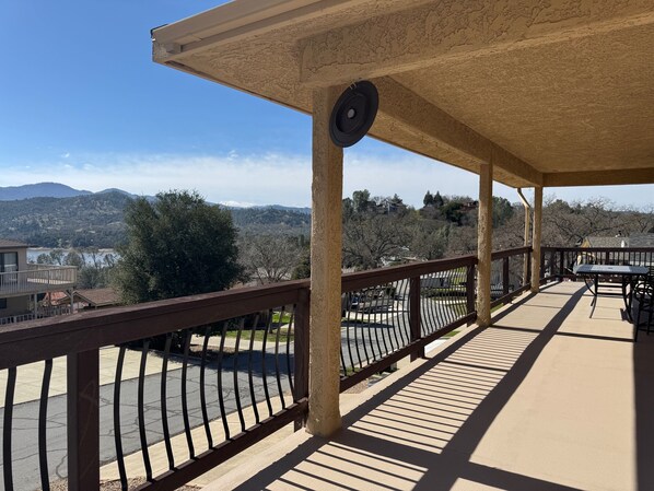 A covered outdoor area with a view of a hilly landscape, a metal railing, and a table with chairs.
