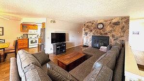 A living room with a stone fireplace, a television, and a dining area with wooden cabinets. - Circle Oak Lake View Family Home (Bradley)