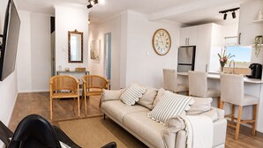 A modern living room with a sofa, chairs, a flat-screen TV, a dining area, and a kitchen. - Cronulla Ocean View, Steps to Beach (Cronulla)