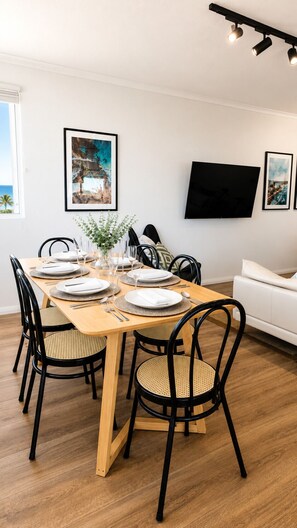 A dining area with a wooden table set for four, black chairs with woven seats, a vase with greenery, and artwork on the walls.
