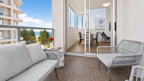 A balcony with a sofa, two chairs, a table, and a view of the ocean. - Cronulla Ocean View, Steps to Beach (Cronulla)