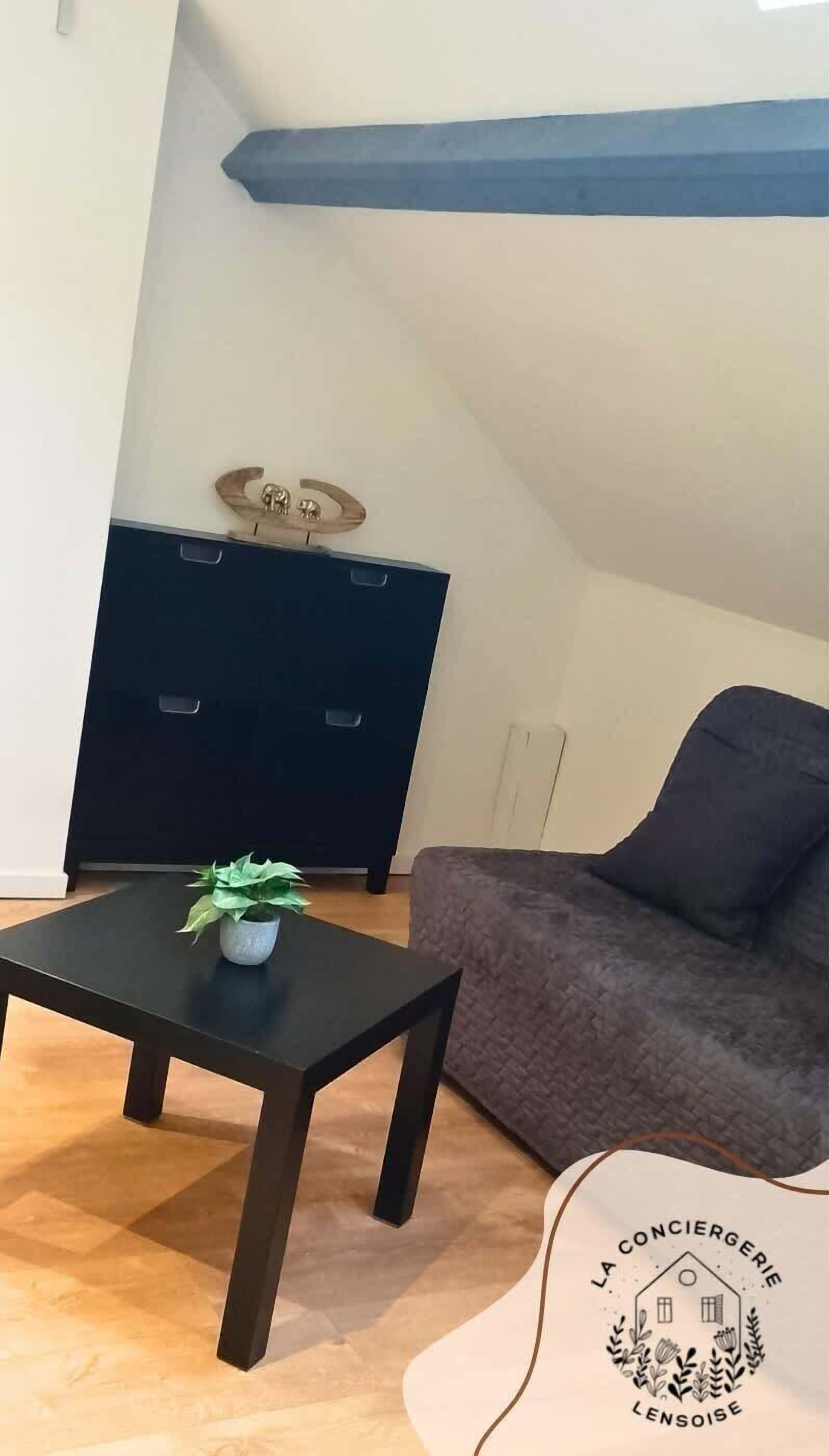 Ett vardagsrum med ett mörkt träbord, en grå soffa och ett svart skåp.