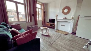 A living room with a sofa, a television, a fireplace, and a view of the outside.
