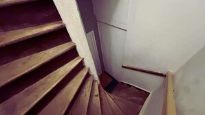 A wooden staircase with a handrail, leading to a landing with a white wall and a door.