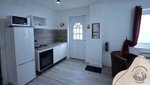 Cocina compacta con microondas, horno y lavabo. Se ve una puerta con ventanal, una silla y un perchero.