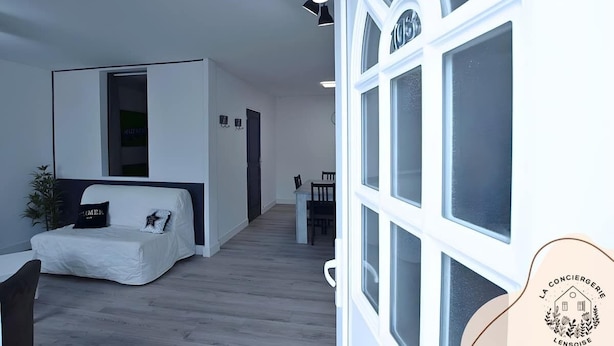 Una habitación moderna y minimalista con una cama, una mesita y una silla. Se ve una ventana con vistas al exterior.