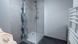 Un baño moderno con cabina de ducha de vidrio, toallero blanco y piso de baldosas.