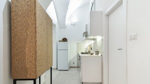A narrow hallway with a corkboard on the left, a white refrigerator, and a kitchen area with a sink and cabinets.