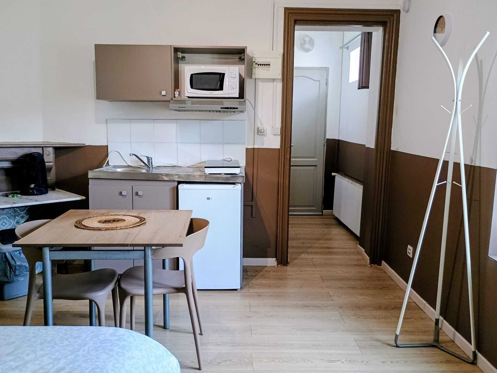 Een compacte keuken met een magnetron, een kleine koelkast, een spoelbak en een eethoek met een tafel en stoelen.