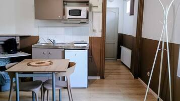 Een compacte keuken met een magnetron, een kleine koelkast, een spoelbak en een eethoek met een tafel en stoelen.