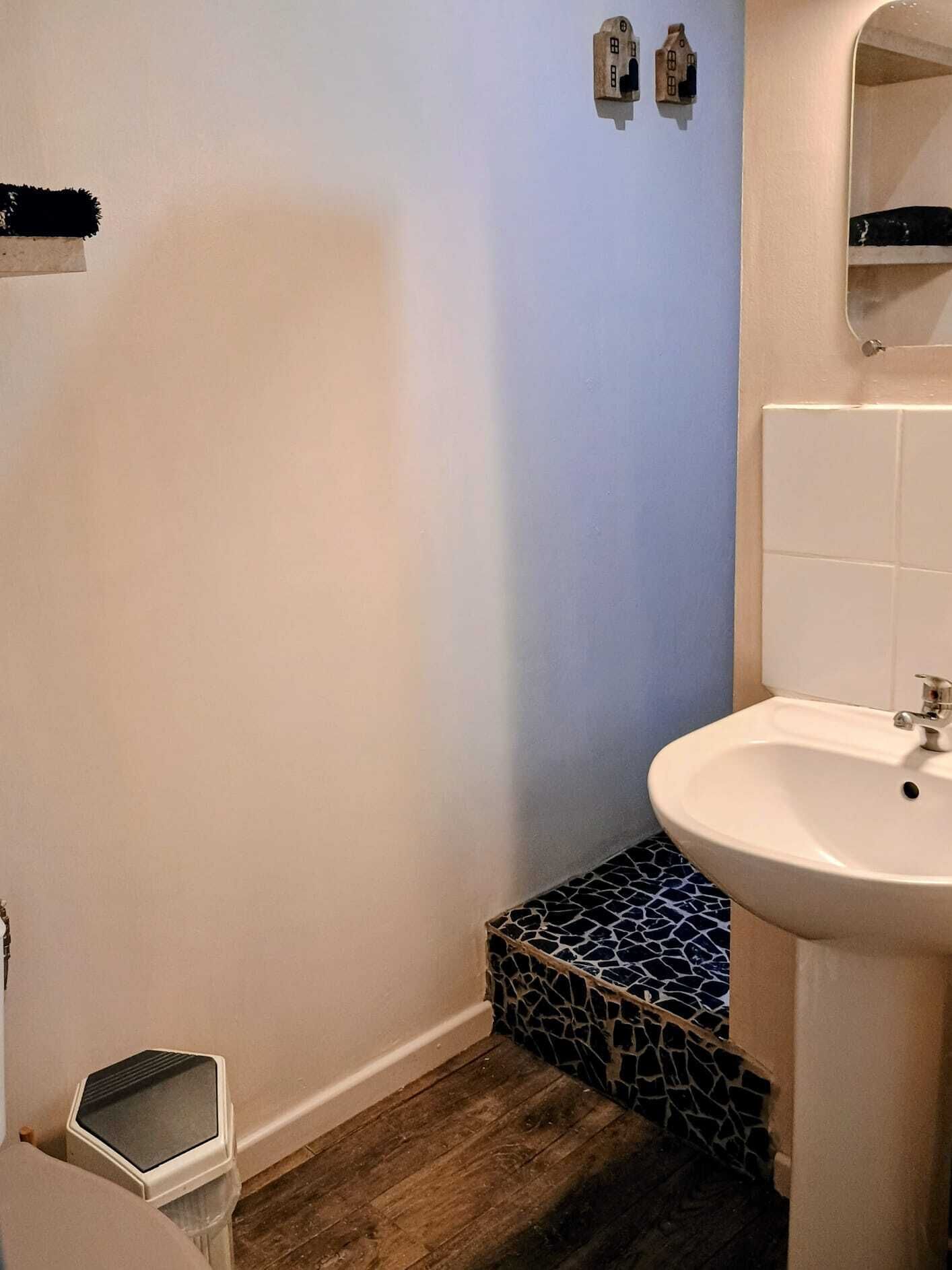 Een badkamer met een wit wastafel, een klein afvalbakje, een betegelde vloer en een blauwe wand.
