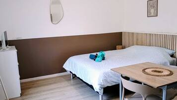 Een slaapkamer met een bed, een bureau, een stoel, een spiegel en een klein kastje.