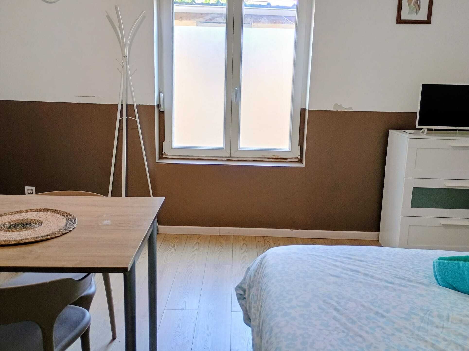 Een kamer met een bed, een bureau, een stoel, een raam en een televisie op een standaard.
