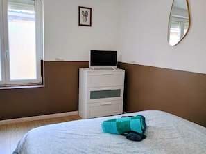 Een slaapkamer met een bed, een bureau met een computer, een raam en een spiegel.