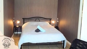A neatly made bed with a white bedspread and two rolled towels, a small table with a lamp, and a chair. - Chez Serge N°102, wifi, parking gratuit, 2pers (Nœux-les-Mines)