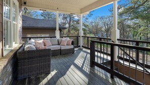 A covered porch with a wicker sofa and a view of the surrounding trees. - Luxury Modern Stay 3BR/2BA Pet Friendly Home Near UAB (Birmingham)