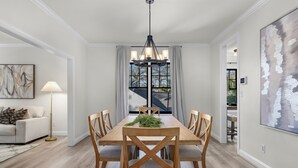 A dining room with a wooden table and chairs, a chandelier, and a view through a window. - Luxury Modern Stay 3BR/2BA Pet Friendly Home Near UAB (Birmingham)