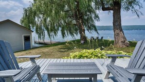 A lakeside deck with Adirondack chairs, a small shed, and a weeping willow tree.