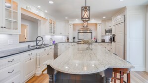 A spacious kitchen with white cabinetry, a large marble island, and modern appliances.