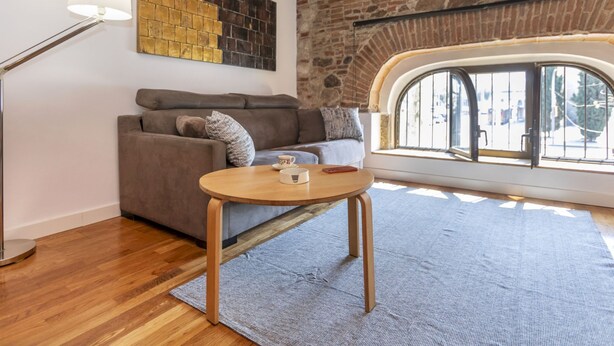 Un salon chaleureux avec un mur en pierre, un plafond en bois, un canapé, une table basse et une lampe.