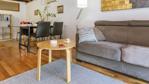 Un salon chaleureux avec un plancher en bois, un canapé gris, une table basse ronde et un coin repas comprenant une table et des chaises.