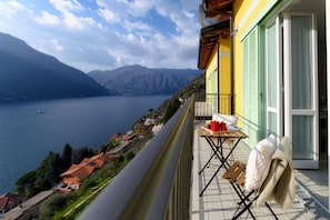 A balcony with a table, chairs, and a view of a lake and mountains.