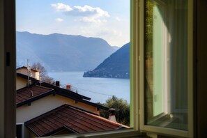 A view through a window of a building overlooking a lake with mountains in the distance. - Nesso Mosaic - MyHomeinComo (Nesso)