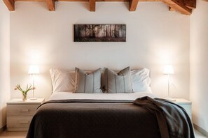 Une chambre à coucher comprenant un lit, deux tables de chevet, une lampe de chevet, un tableau accroché au mur et un plafond en bois.