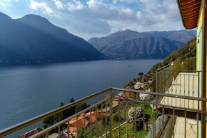 A balcony with a view of a lake and mountains, a railing, and a small table.