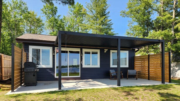 A covered patio area with a grill, seating, and a view of a lake.