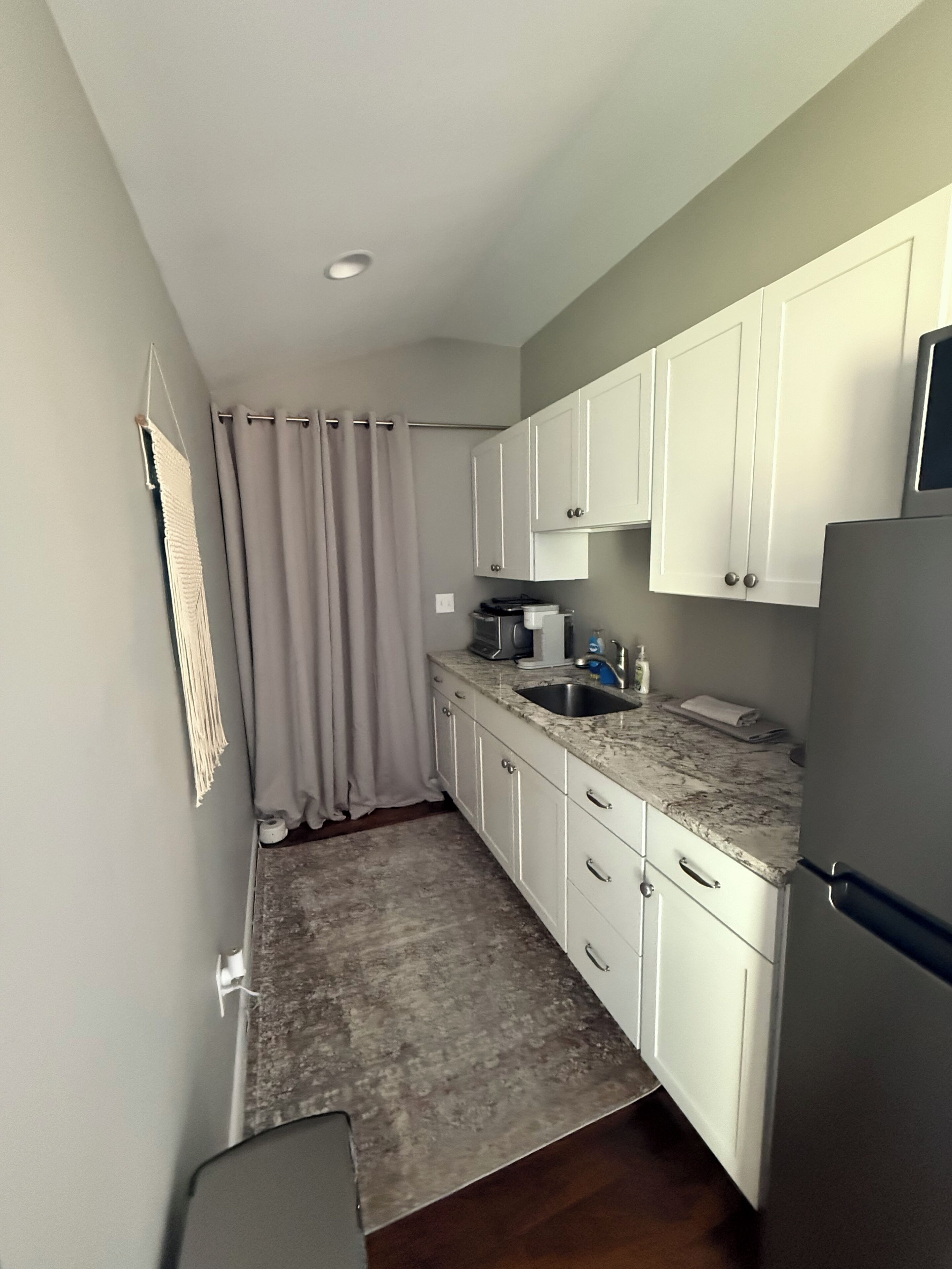 A compact kitchen with white cabinets, a granite countertop, a built-in sink, and a refrigerator.