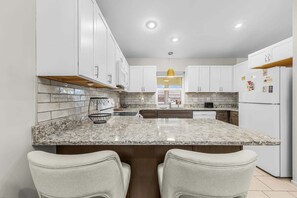Una cocina moderna con armarios blancos, encimera de granito y dos taburetes de bar.