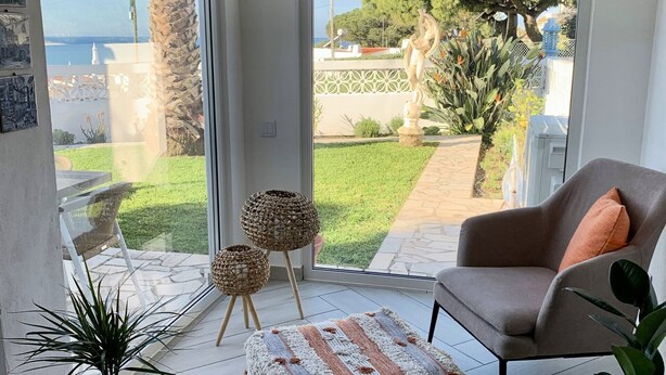 A modern living room with a large sliding glass door leading to a patio. There is a grey sofa, a small round table, and a potted plant. - Casa Leon - 2 bed apartment with stunning sea views & superb location (Carvoeiro)