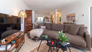 A modern living room with a sofa, coffee table, and TV stand. There is a kitchen in the background with a dining area. - Casa Leon - 2 bed apartment with stunning sea views & superb location (Carvoeiro)