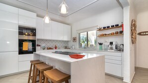 A modern kitchen with white cabinetry, a central island with stools, pendant lighting, and a view to the outdoors. - Casa Leon - 2 bed apartment with stunning sea views & superb location (Carvoeiro)