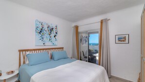 A bedroom with a bed, a small table, a painting, and a view through a glass door. - Casa Leon - 2 bed apartment with stunning sea views & superb location (Carvoeiro)