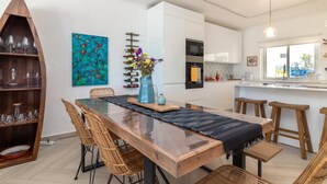 A modern kitchen with white cabinets, a wooden dining table, wicker chairs, and a blue vase with flowers. - Casa Leon - 2 bed apartment with stunning sea views & superb location (Carvoeiro)