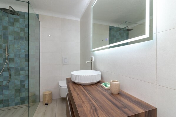 A modern bathroom with a glass-enclosed shower, a round white sink, and a wooden vanity.