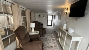 Ein geräumiges Wohnzimmer mit einem großen Flachbildfernseher, einer Couch, einem Couchtisch und einem Konsolentisch mit Dekorationselementen.