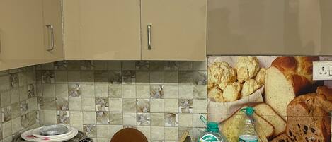 Una cocina con armarios color beige, salpicadero de azulejos y encimera de granito. Hay varios utensilios y objetos de cocina sobre la encimera.