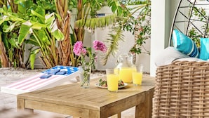 Uma mesa de madeira com uma bandeja de itens listrados em azul e branco, um jarro de suco de laranja e um vaso com flores cor-de-rosa.