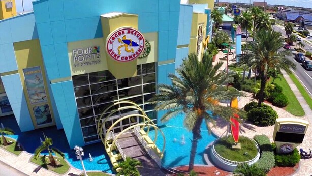 A hotel with a large pool, palm trees, and a sign reading "FOUR POINTS." - Cocoa Beach Condo - SeaBreeze (Cocoa Beach)