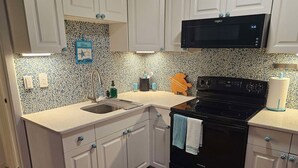 A kitchen with white cabinets, a black stove, a microwave, and a tiled backsplash. - Cocoa Beach Condo - SeaBreeze (Cocoa Beach)